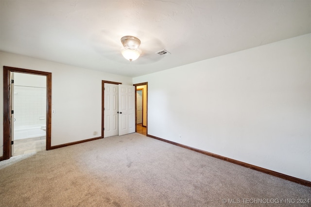 unfurnished bedroom with light colored carpet, baseboards, and ensuite bathroom