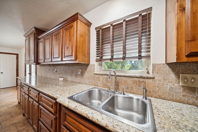 kitchen featuring a sink, decorative backsplash, brown cabinetry, and light stone counters