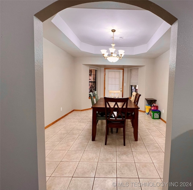 dining space with a tray ceiling, a chandelier, and light tile patterned floors