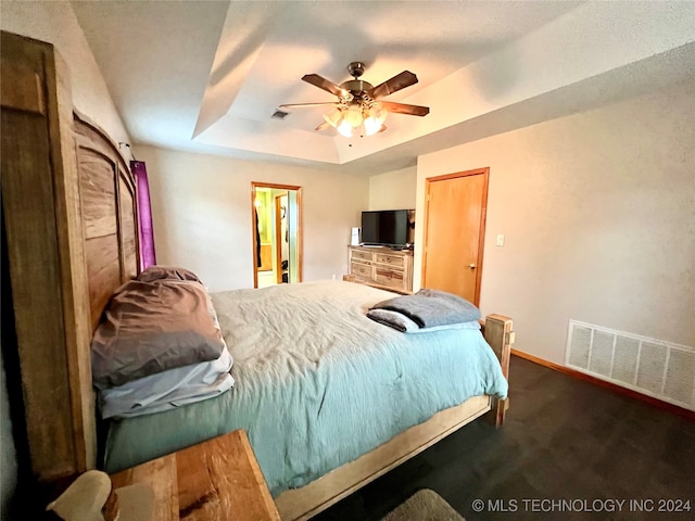 bedroom featuring a tray ceiling, dark colored carpet, and ceiling fan