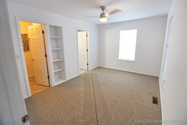 unfurnished bedroom featuring a walk in closet, light carpet, a closet, and ceiling fan