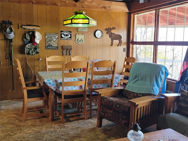 carpeted dining space featuring wooden walls