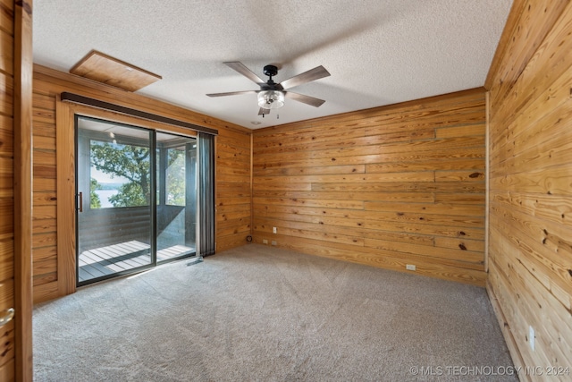 carpeted spare room with ceiling fan, a textured ceiling, and wooden walls