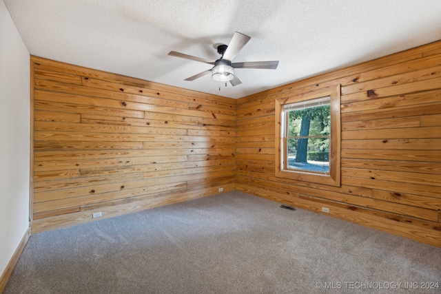 spare room featuring ceiling fan, a textured ceiling, wood walls, and carpet flooring