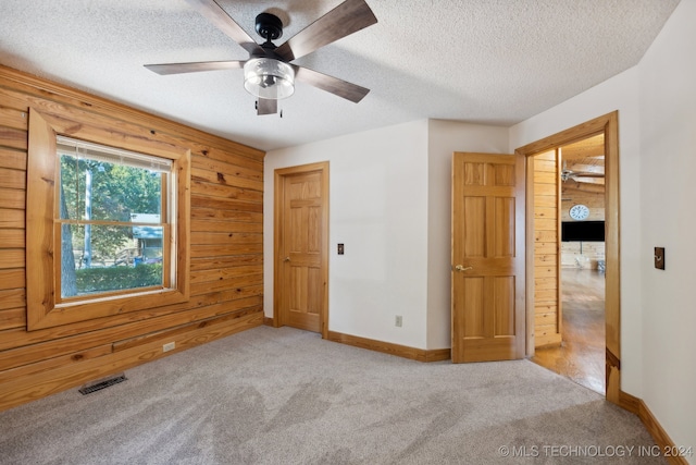 unfurnished bedroom featuring wood walls, ceiling fan, light colored carpet, a closet, and a textured ceiling