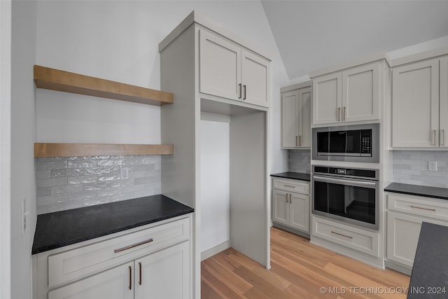 kitchen with appliances with stainless steel finishes, decorative backsplash, white cabinets, light wood-type flooring, and lofted ceiling