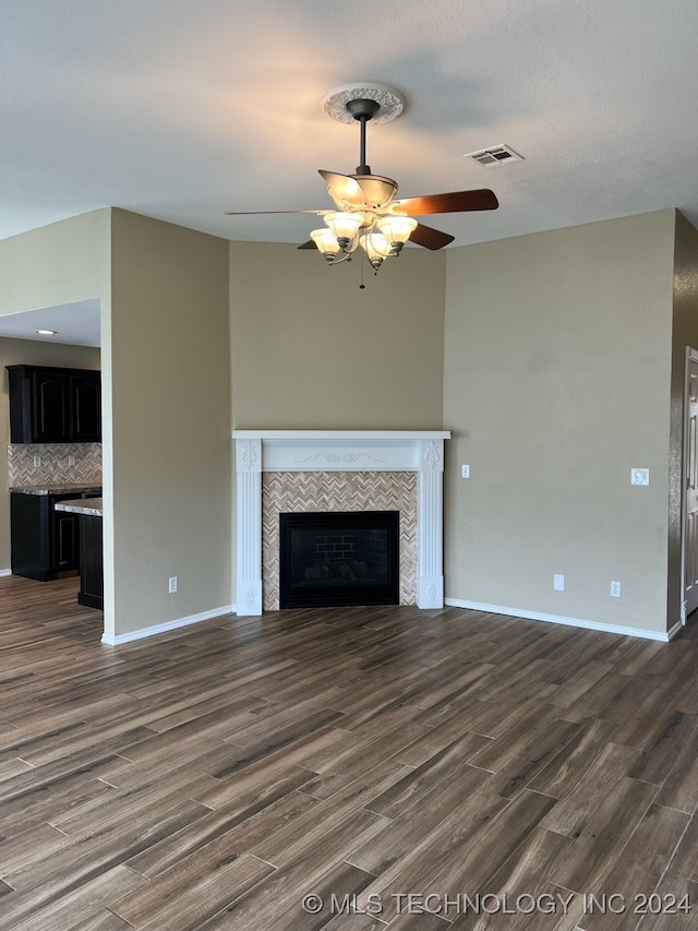 unfurnished living room with a textured ceiling, a tile fireplace, ceiling fan, and dark wood-type flooring