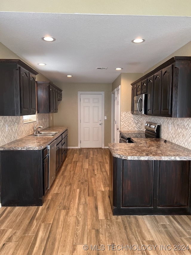 kitchen featuring appliances with stainless steel finishes, decorative backsplash, dark brown cabinets, light hardwood / wood-style flooring, and sink