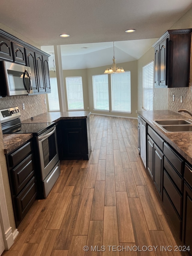 kitchen with decorative backsplash, stainless steel appliances, hardwood / wood-style flooring, sink, and a notable chandelier