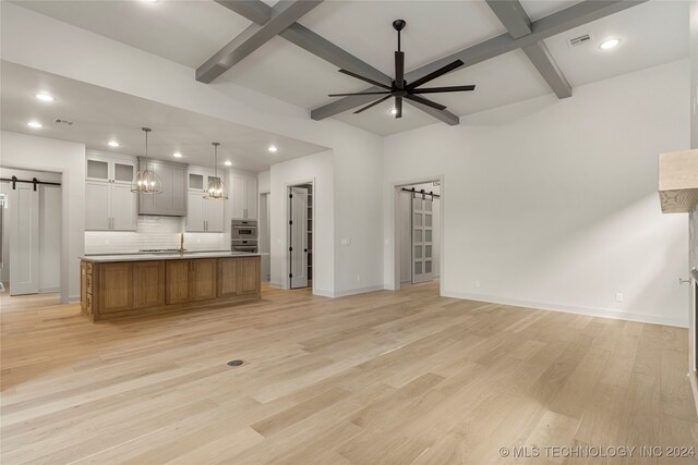 kitchen featuring ceiling fan, a barn door, a spacious island, light hardwood / wood-style floors, and decorative backsplash