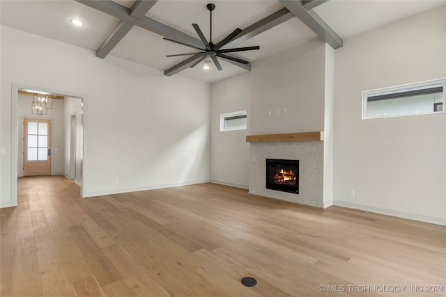 unfurnished living room with light hardwood / wood-style floors, ceiling fan with notable chandelier, a fireplace, and beam ceiling