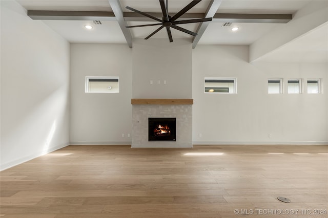 unfurnished living room with light hardwood / wood-style flooring, a tiled fireplace, and beamed ceiling