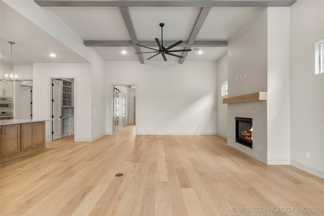 unfurnished living room with ceiling fan with notable chandelier, a tiled fireplace, and light hardwood / wood-style floors