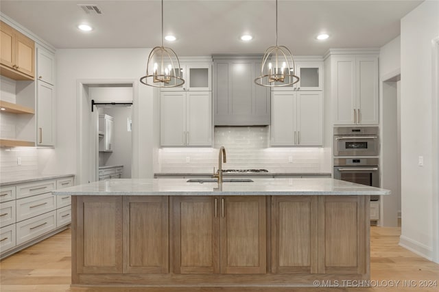 kitchen with double oven, sink, an island with sink, and light stone counters