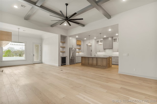 unfurnished living room featuring light hardwood / wood-style floors, beamed ceiling, sink, ceiling fan with notable chandelier, and beverage cooler