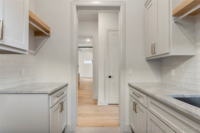 kitchen featuring backsplash, light stone countertops, light hardwood / wood-style flooring, and white cabinets