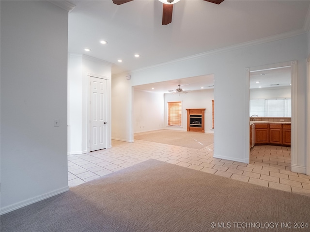 unfurnished living room with ceiling fan, sink, crown molding, and light tile patterned floors