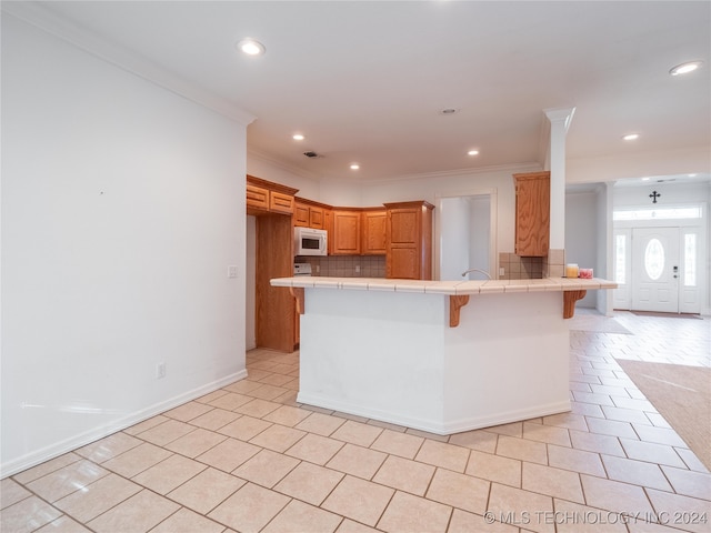 kitchen with a kitchen breakfast bar, backsplash, kitchen peninsula, crown molding, and tile counters