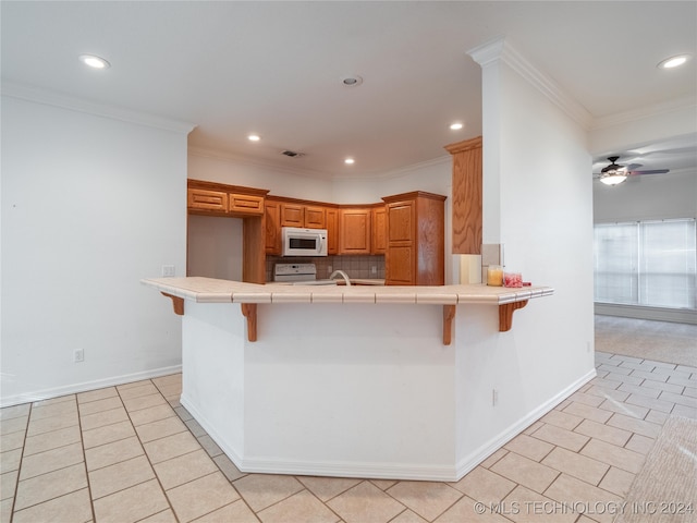 kitchen with a kitchen bar, white appliances, kitchen peninsula, and tile countertops