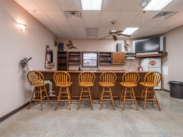 kitchen featuring white refrigerator, ceiling fan, a kitchen bar, and a paneled ceiling