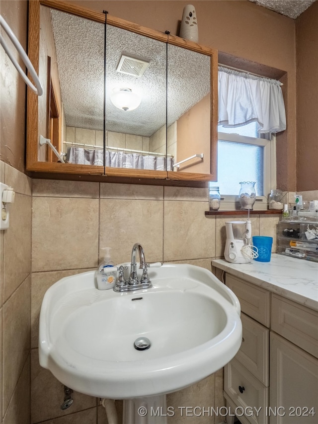 bathroom featuring a textured ceiling, tile walls, and sink