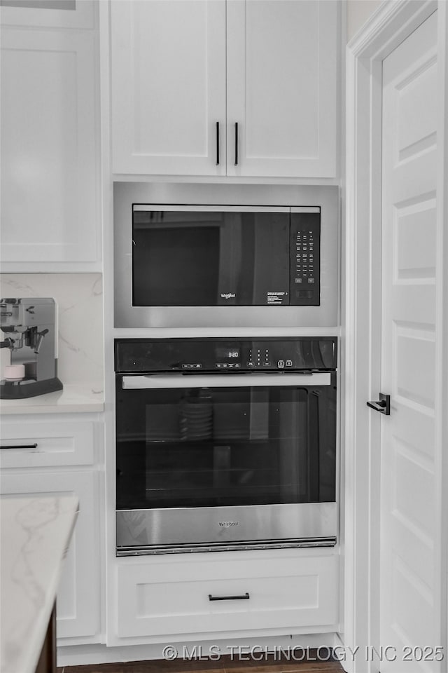 room details with built in microwave, stainless steel oven, light stone counters, and white cabinets