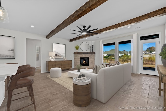 living room with beamed ceiling, ceiling fan, and a fireplace