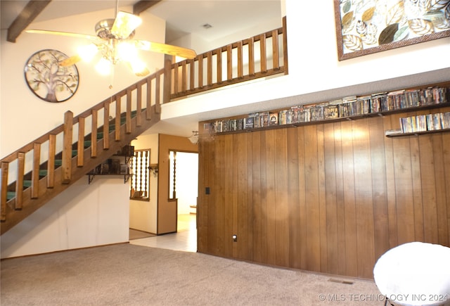 carpeted living area with wood walls, stairway, a high ceiling, and ceiling fan