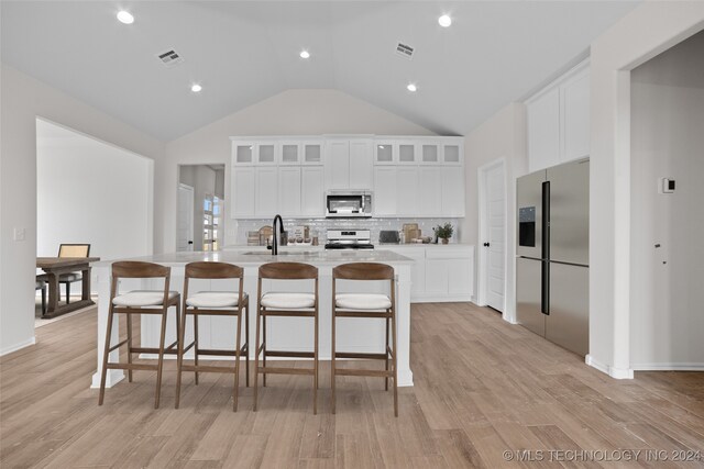 kitchen featuring white cabinets, a kitchen island with sink, a kitchen bar, light hardwood / wood-style flooring, and stainless steel appliances