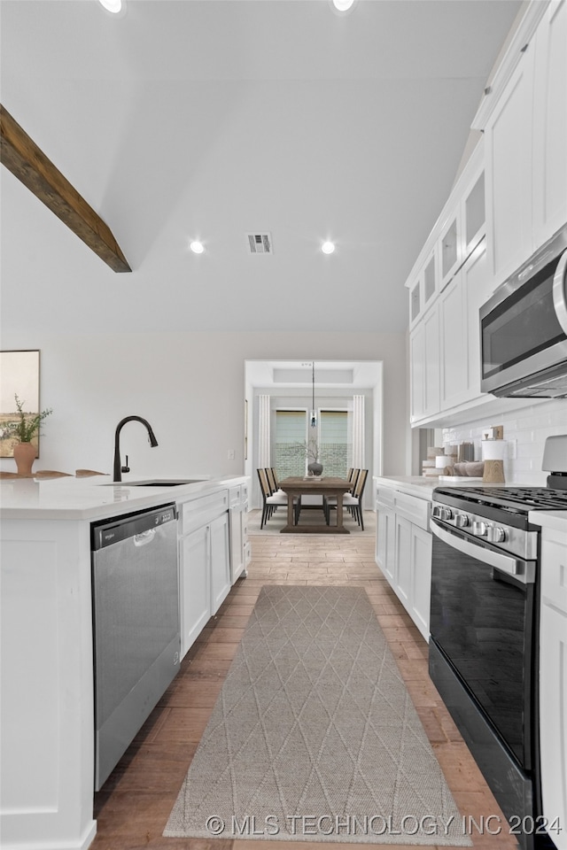 kitchen featuring white cabinetry, lofted ceiling with beams, appliances with stainless steel finishes, and light hardwood / wood-style flooring