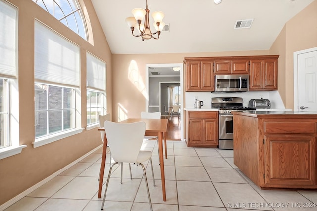 kitchen with decorative light fixtures, stainless steel appliances, light tile patterned floors, and lofted ceiling