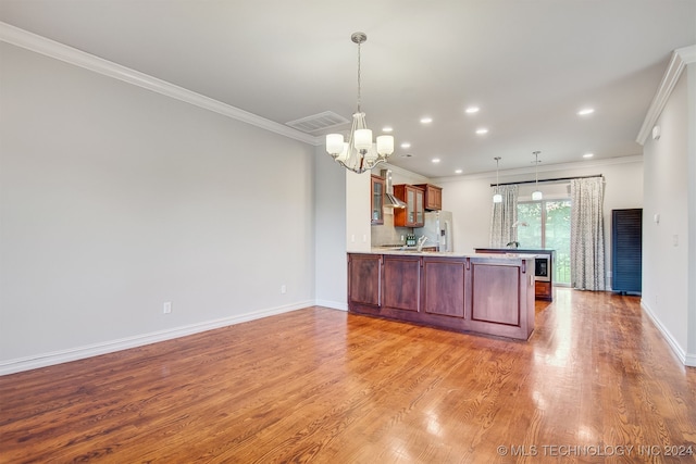 kitchen featuring light hardwood / wood-style floors, wall chimney exhaust hood, kitchen peninsula, ornamental molding, and a notable chandelier