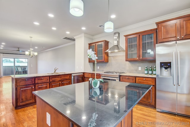 kitchen featuring appliances with stainless steel finishes, hanging light fixtures, a kitchen island, and wall chimney range hood