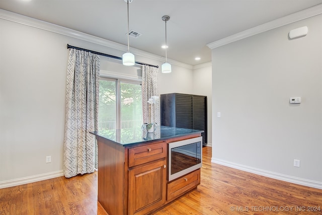 kitchen with stainless steel microwave, light wood-type flooring, hanging light fixtures, and ornamental molding