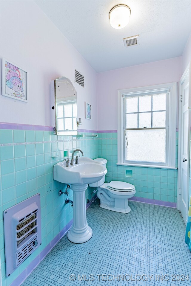 bathroom featuring tile walls, toilet, heating unit, and plenty of natural light