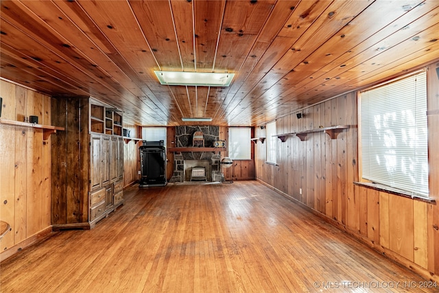 interior space with a stone fireplace, light hardwood / wood-style flooring, wood walls, and wood ceiling