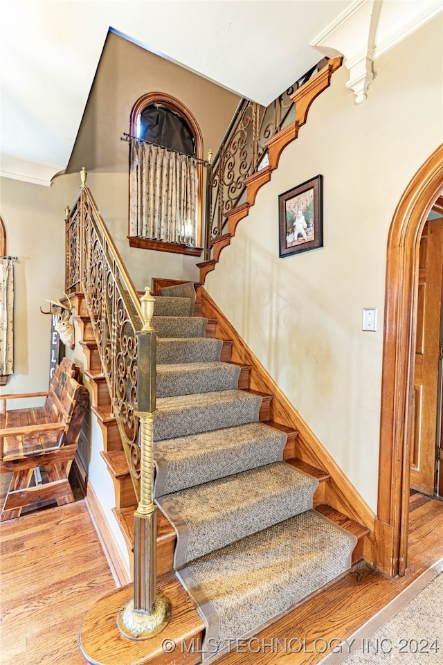 stairs with ornamental molding and hardwood / wood-style floors