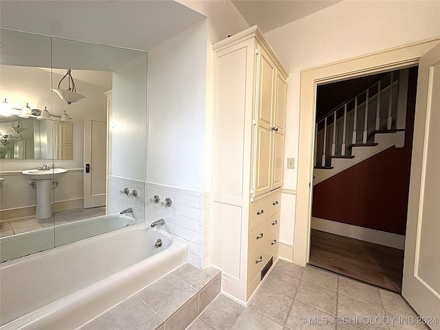 bathroom with tile patterned flooring, sink, and tiled bath