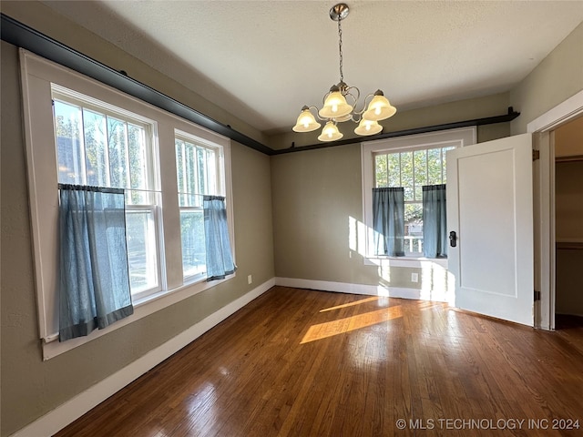 unfurnished dining area featuring a chandelier, wood-type flooring, and a textured ceiling