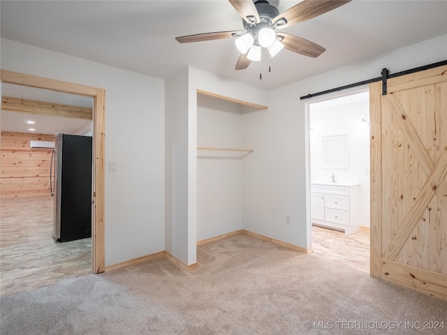 unfurnished bedroom with a barn door, stainless steel refrigerator, a closet, ceiling fan, and light colored carpet