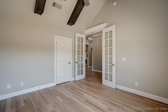 empty room with high vaulted ceiling, a chandelier, light hardwood / wood-style floors, and french doors