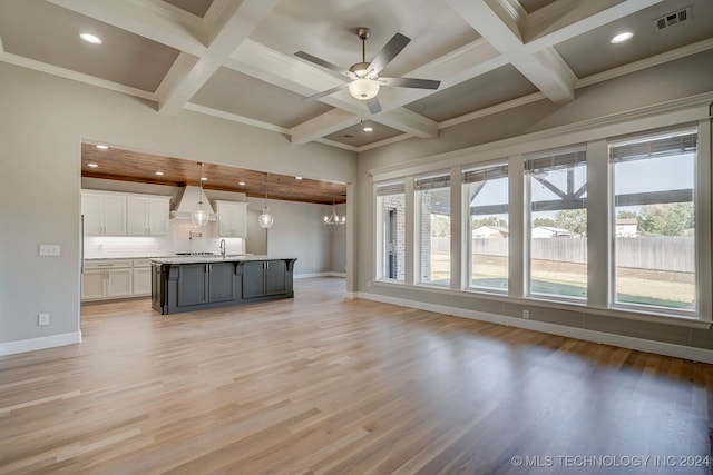 unfurnished living room featuring ceiling fan with notable chandelier, light hardwood / wood-style floors, ornamental molding, and beamed ceiling