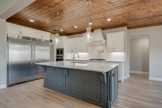 kitchen with pendant lighting, custom exhaust hood, sink, white cabinetry, and built in appliances