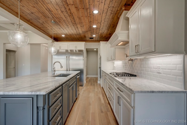 kitchen with light wood-type flooring, sink, hanging light fixtures, custom exhaust hood, and stainless steel appliances