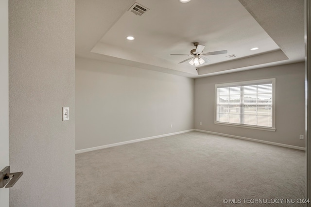 unfurnished room featuring a raised ceiling, ceiling fan, and light colored carpet