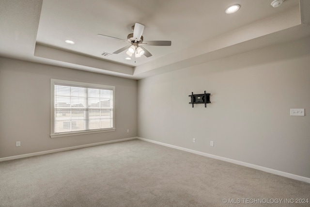 carpeted empty room featuring ceiling fan and a raised ceiling