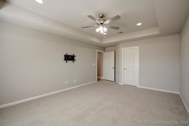 unfurnished bedroom featuring light carpet, a tray ceiling, and ceiling fan