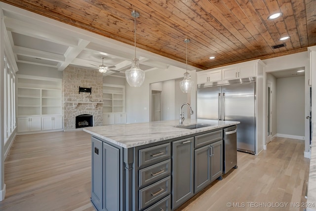 kitchen featuring white cabinets, hanging light fixtures, sink, built in features, and a center island with sink