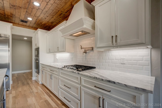 kitchen featuring light hardwood / wood-style floors, white cabinets, custom exhaust hood, backsplash, and appliances with stainless steel finishes