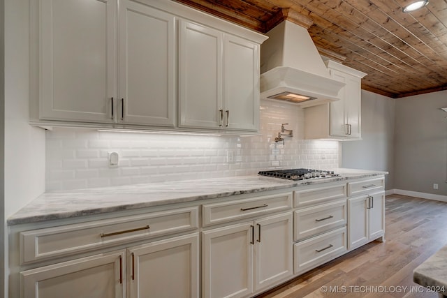 kitchen with white cabinets, premium range hood, tasteful backsplash, stainless steel gas stovetop, and light hardwood / wood-style floors